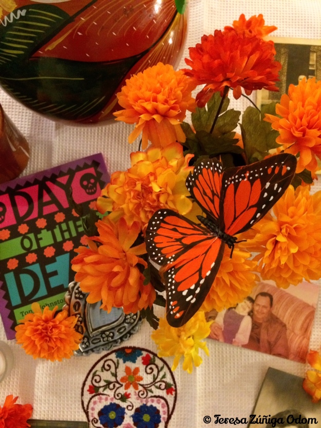 Some of the items on my Day of the Dead living room altar include a Day of the Dead book, carnations, butterflies and photos...